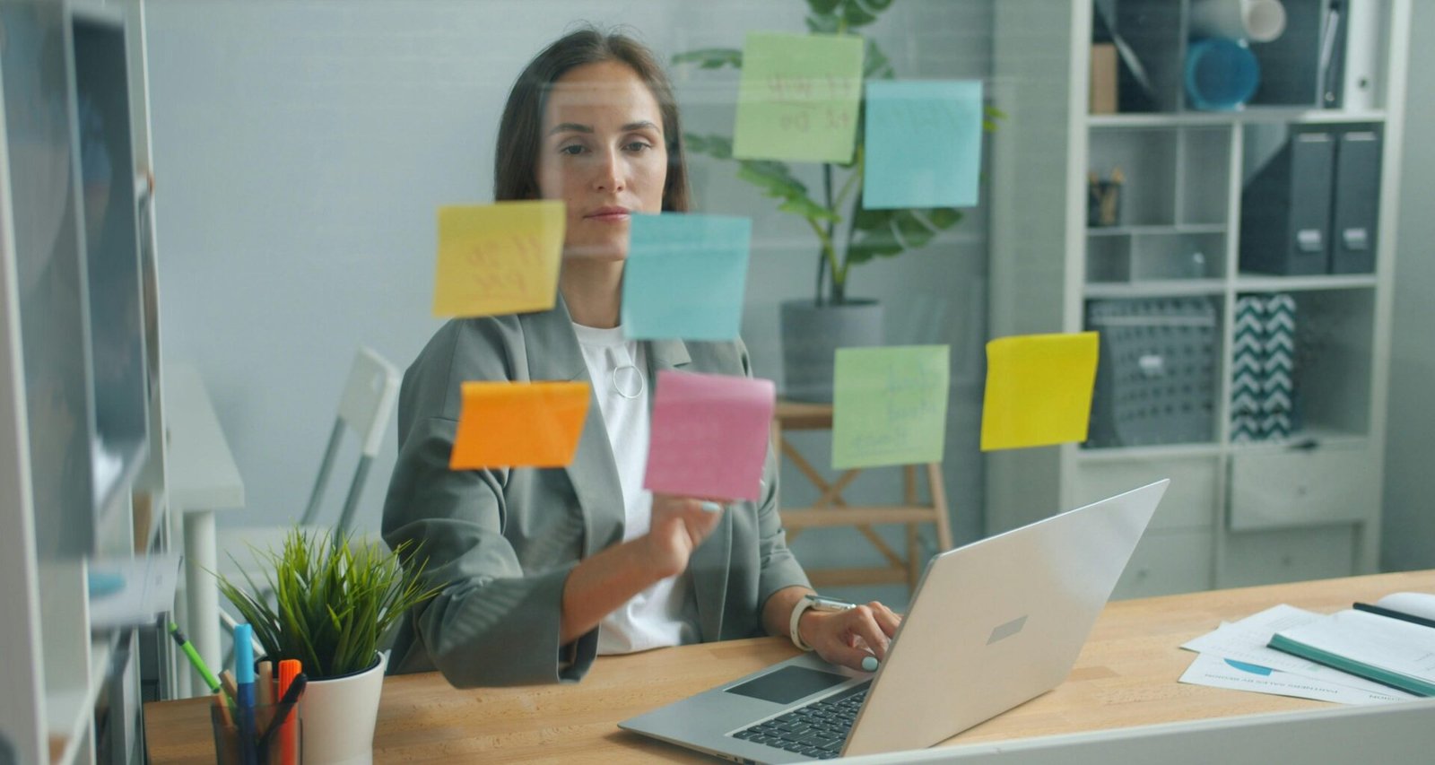 Frau ordnet bunte Haftnotizen auf einer Glaswand für Brainstorming und Projektplanung im modernen Büro.