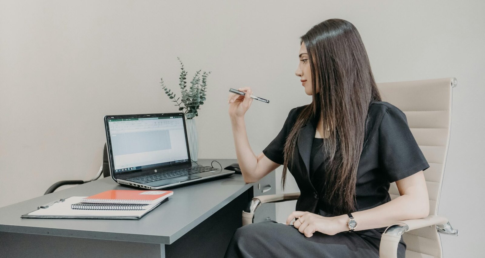 Frau sitzt an einem Schreibtisch und arbeitet am Laptop, umgeben von Arbeitsunterlagen und modernen Büromaterialien