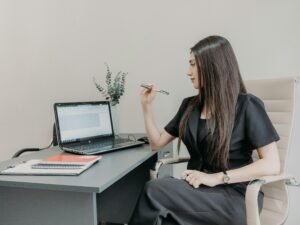 Frau sitzt an einem Schreibtisch und arbeitet am Laptop, umgeben von Arbeitsunterlagen und modernen Büromaterialien