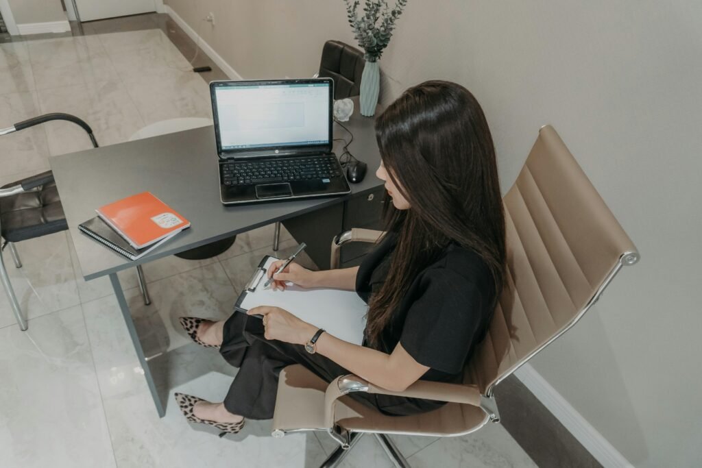 Frau arbeitet an einem Schreibtisch mit Laptop und Notizbuch, konzentriert auf ihre Aufgaben im modernen Arbeitsumfeld
