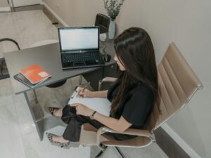 Frau arbeitet an einem Schreibtisch mit Laptop und Notizbuch, konzentriert auf ihre Aufgaben im modernen Arbeitsumfeld