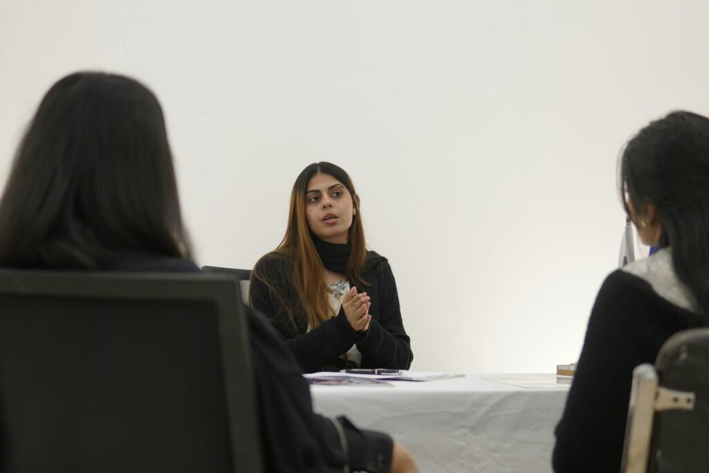 Frau spricht mit zwei Personen an einem Tisch in einem modernen Büro während eines Meetings.