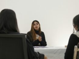 Frau spricht mit zwei Personen an einem Tisch in einem modernen Büro während eines Meetings.