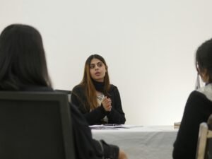 Frau spricht mit zwei Personen an einem Tisch in einem modernen Büro während eines Meetings.