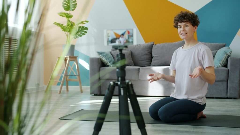 Eine Frau filmt sich im eigenen Wohnzimmer mit einer Kamera auf einem Stativ für einen Videodreh