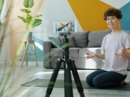 Eine Frau filmt sich im eigenen Wohnzimmer mit einer Kamera auf einem Stativ für einen Videodreh