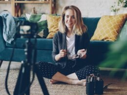 Frau sitzt im Wohnzimmer und nimmt mit einer Kamera ein Video auf, beispielhaft für moderne Content-Produktion zu Hause