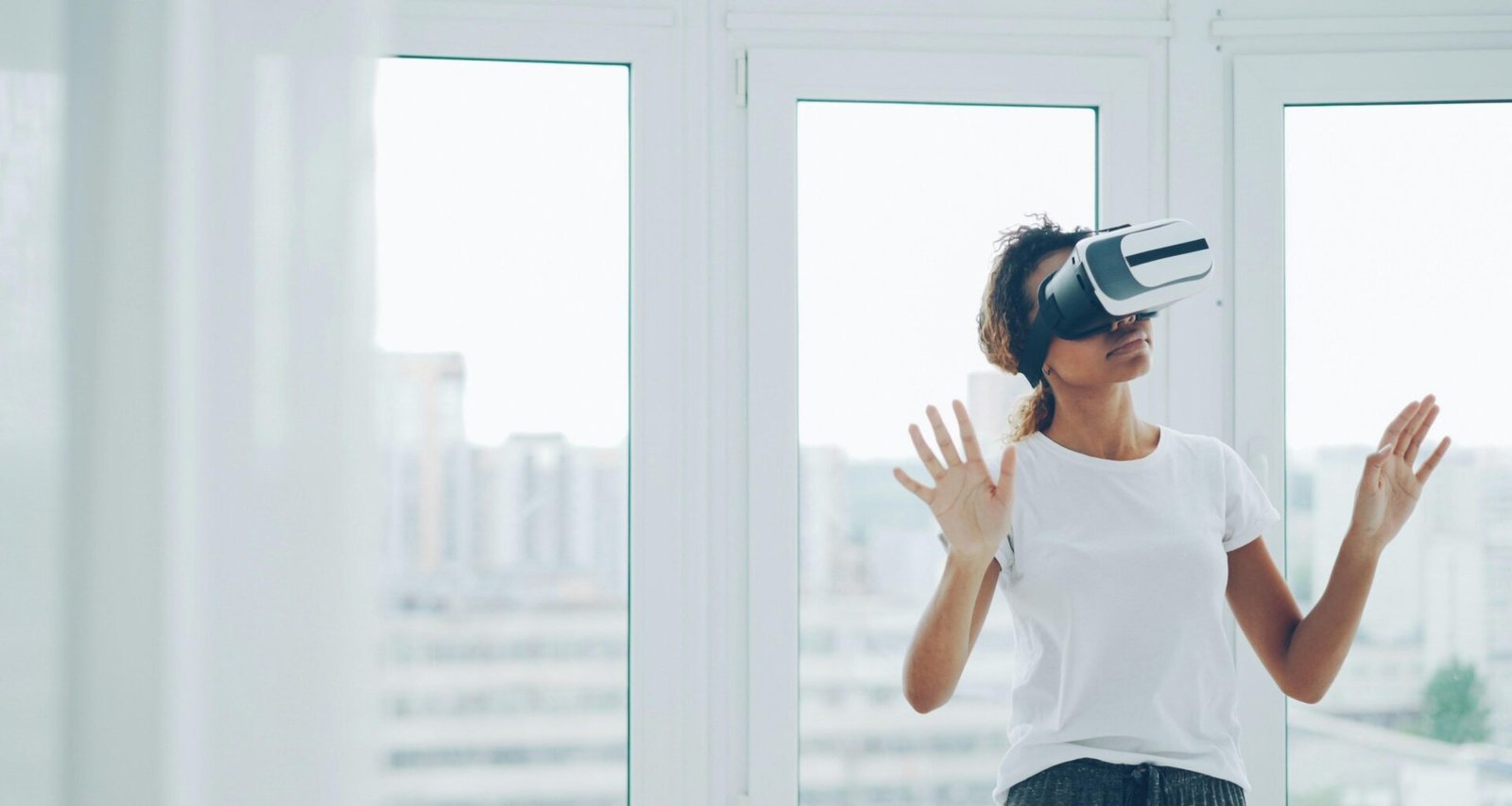 Frau mit Virtual-Reality-Headset sitzt im Innenraum nahe eines großen Fensters und testet moderne Technologie.
