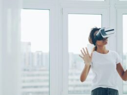 Frau mit Virtual-Reality-Headset sitzt im Innenraum nahe eines großen Fensters und testet moderne Technologie.