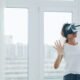 Frau mit Virtual-Reality-Headset sitzt im Innenraum nahe eines großen Fensters und testet moderne Technologie.