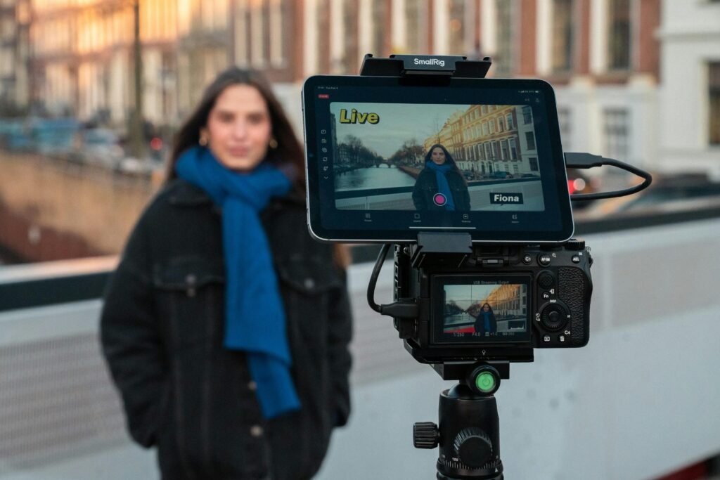 Eine Frau filmt sich eigenständig vor einer Kamera und nutzt dabei zusätzlich ein Tablet zur Unterstützung ihrer Aufnahme.