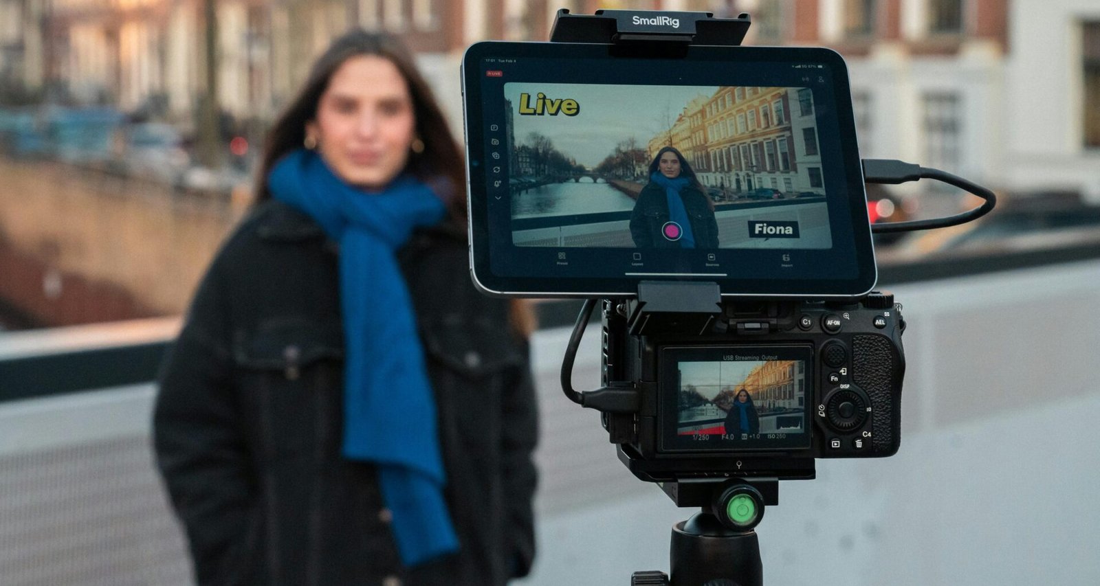 Eine Frau filmt sich eigenständig vor einer Kamera und nutzt dabei zusätzlich ein Tablet zur Unterstützung ihrer Aufnahme.