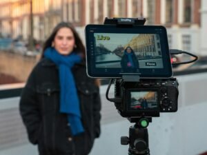 Eine Frau filmt sich eigenständig vor einer Kamera und nutzt dabei zusätzlich ein Tablet zur Unterstützung ihrer Aufnahme.