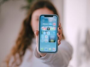 Frau hält ein Smartphone mit deutlich sichtbaren App-Symbolen auf dem Bildschirm, Fokus auf mobile Technologien.