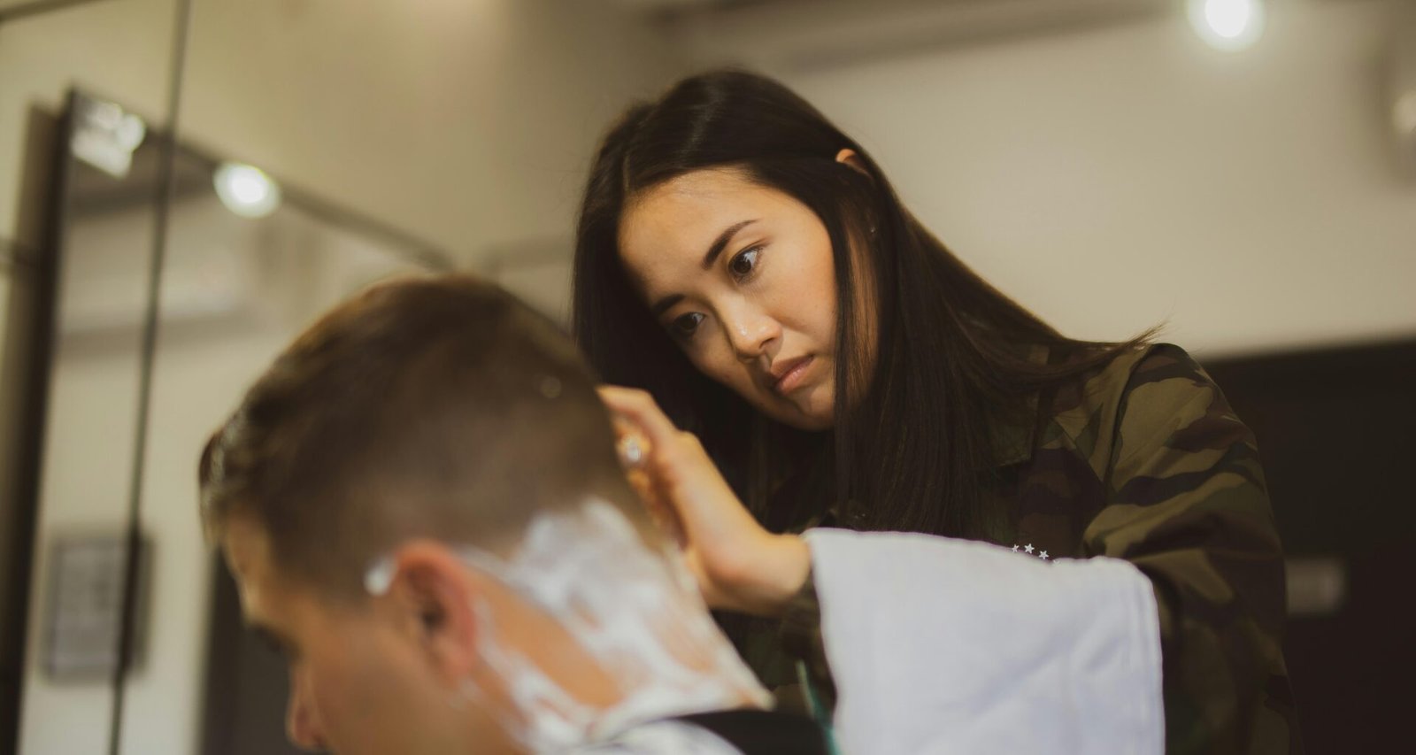 Frau hält ein gerades Rasiermesser und rasiert sorgfältig den Hinterkopf eines Mannes beim Haarschnitt.