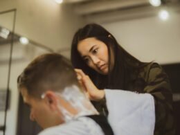 Frau hält ein gerades Rasiermesser und rasiert sorgfältig den Hinterkopf eines Mannes beim Haarschnitt.