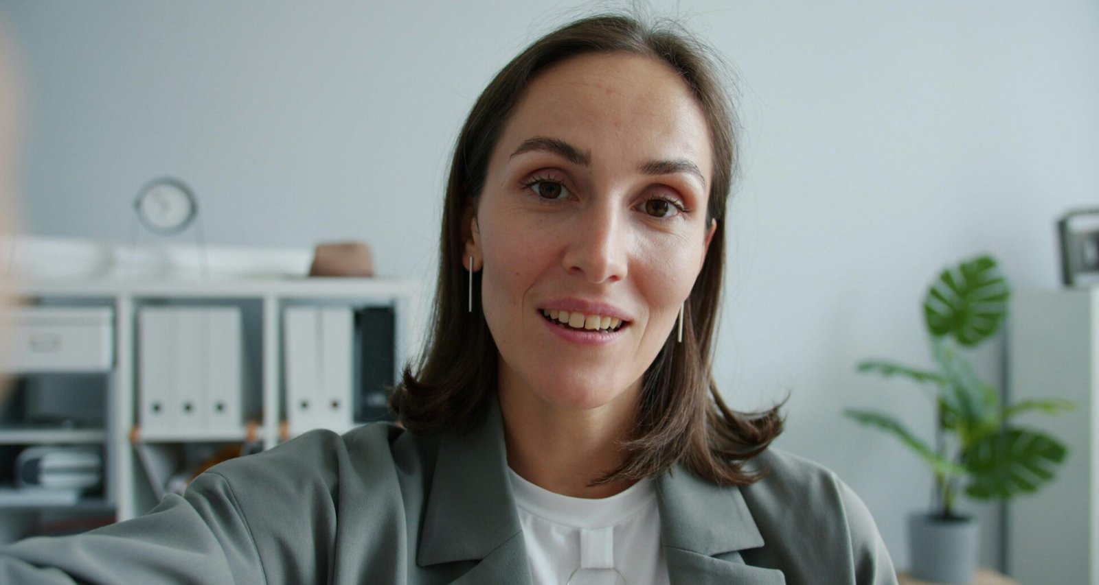 Frau im eleganten Anzug sitzt und schaut direkt in die Kamera, professionelle Business-Atmosphäre