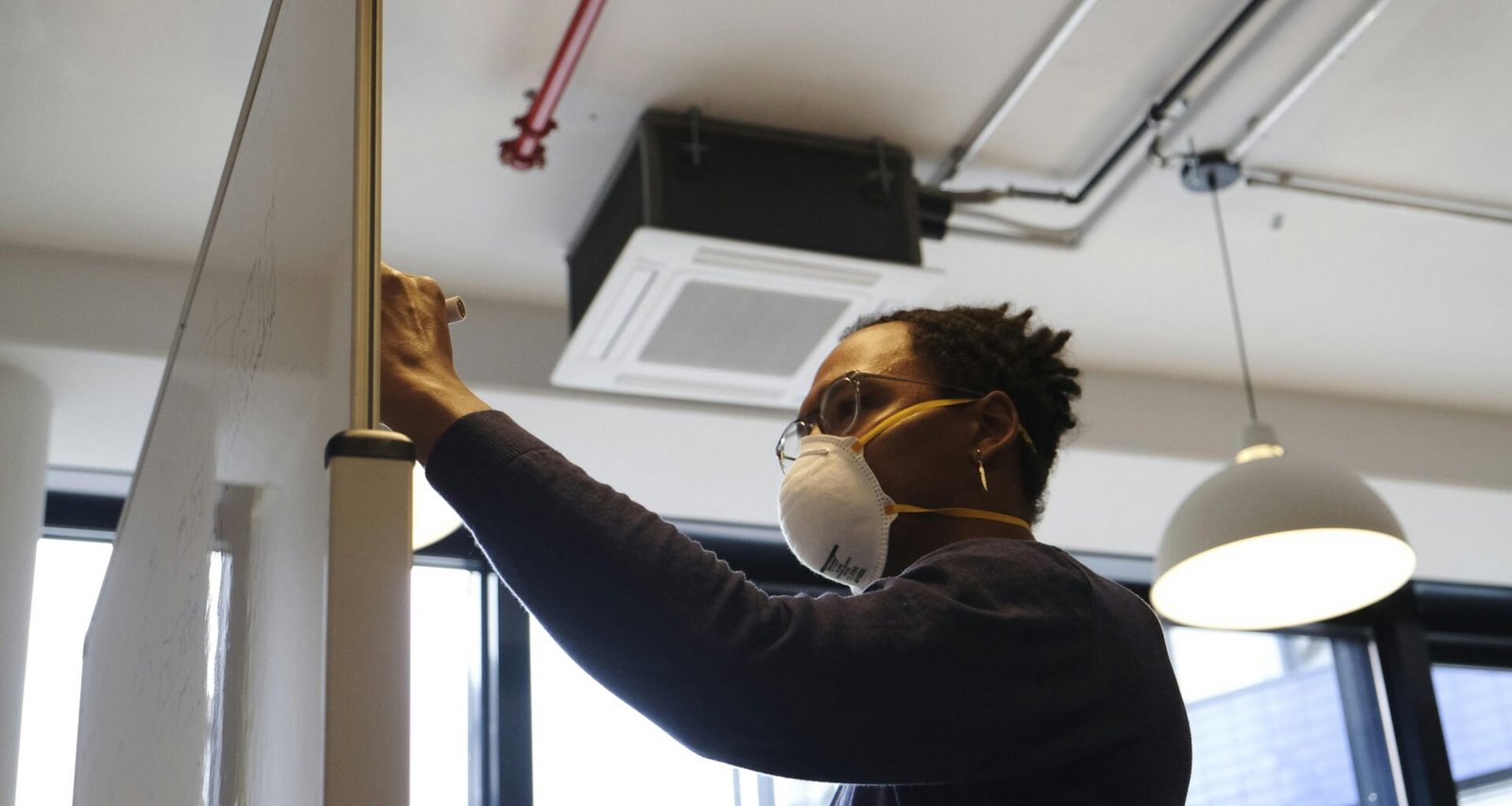 Frau in blauem Langarmshirt mit weißer Schutzbrille arbeitet konzentriert in moderner Umgebung