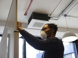 Frau in blauem Langarmshirt mit weißer Schutzbrille arbeitet konzentriert in moderner Umgebung