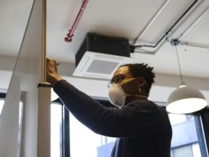 Frau in blauem Langarmshirt mit weißer Schutzbrille arbeitet konzentriert in moderner Umgebung