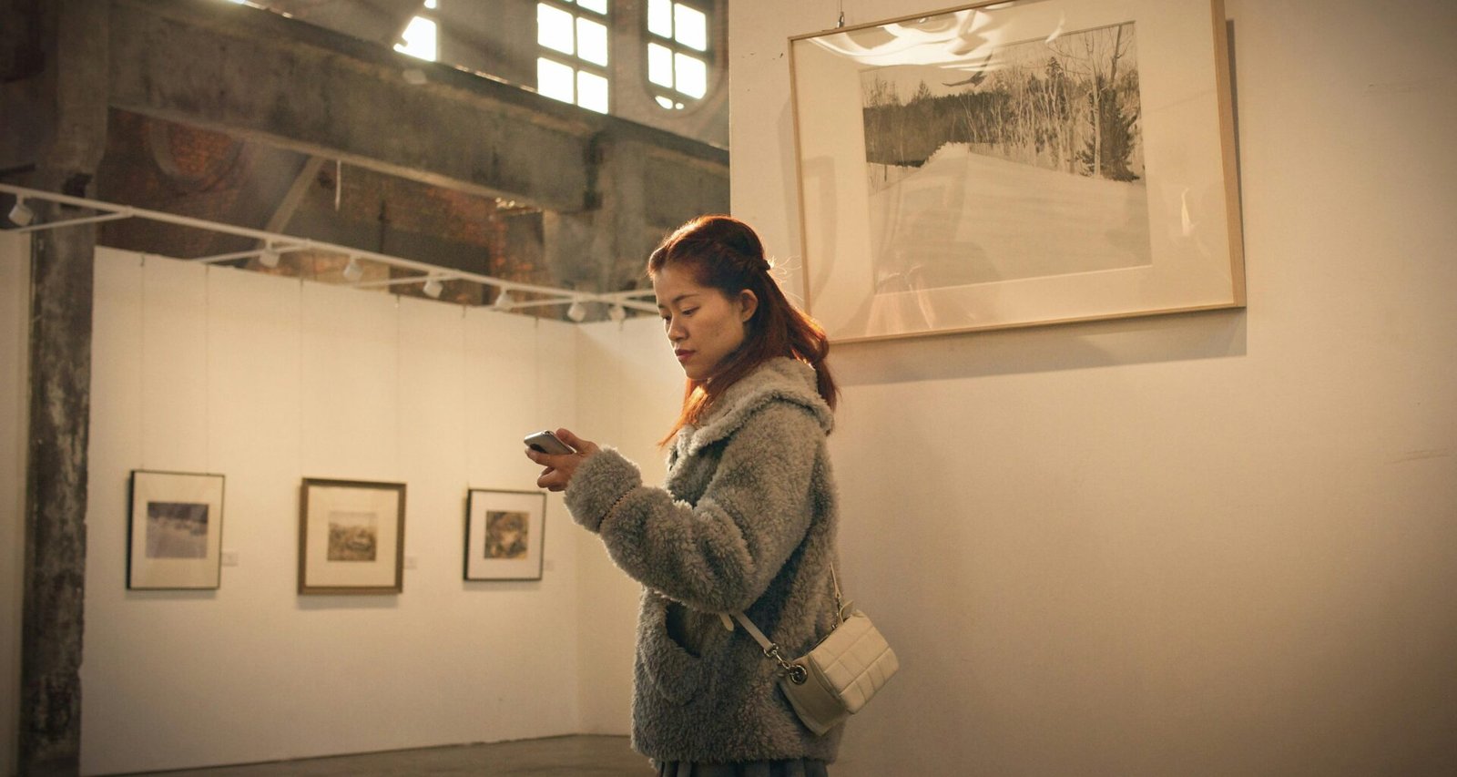 Frau mit grauem Mantel steht vor einer weißen Wand, schlichtes und modernes Motiv für Lifestyle- oder Mode-Artikel