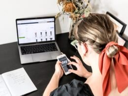 Frau in orangefarbenem Shirt bedient ihr iPhone in heller Umgebung, Fokus auf zeitgemäße Smartphone-Nutzung