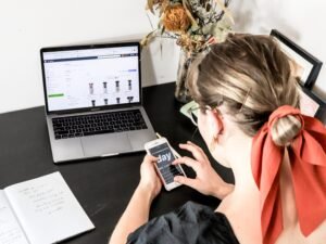 Frau in orangefarbenem Shirt bedient ihr iPhone in heller Umgebung, Fokus auf zeitgemäße Smartphone-Nutzung