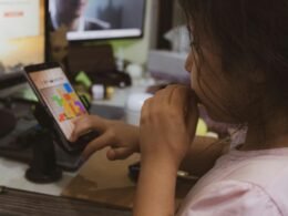 Frau im pinken Shirt hält ein Smartphone in der Hand und nutzt es, Fokus auf mobile Kommunikation im Alltag