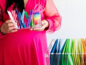 Frau im pinken Kleid hält farbige Stifte und eine Schere in der Hand, Nahaufnahme am Schreibtisch