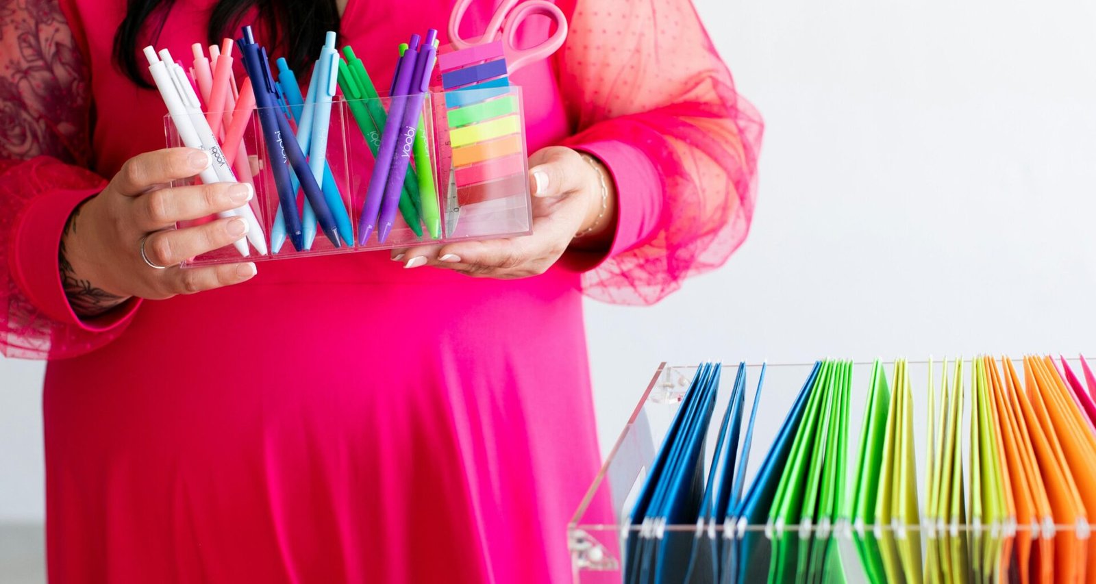 Frau im pinken Kleid hält verschiedene bunte Stifte und eine Schere in einer hellen Umgebung