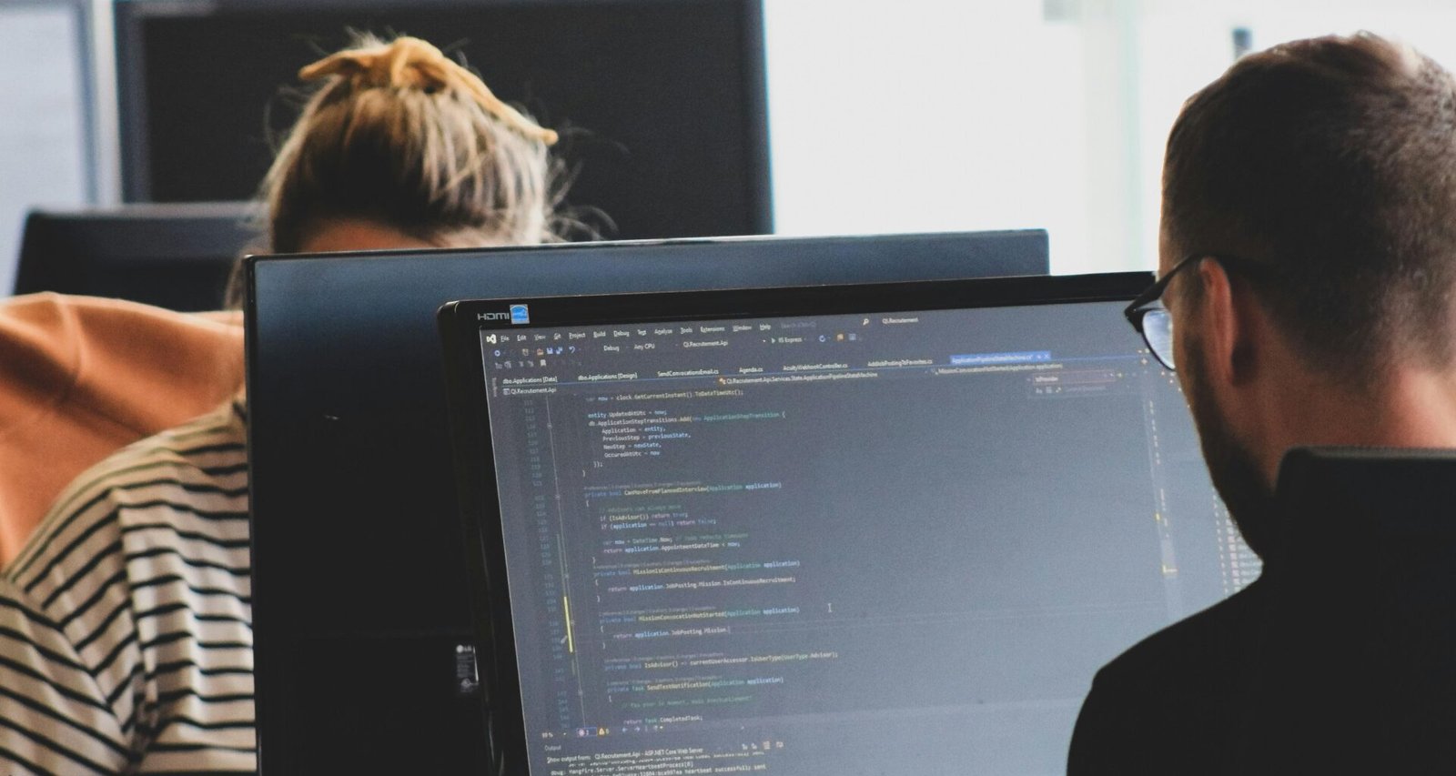 Frau in schwarzem Shirt sitzt am Schreibtisch neben einem großen, schwarzen Monitor in einem modernen Büro.