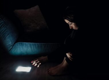 Frau mit schwarzen langen Ärmeln sitzt auf einem blauen Sofa und arbeitet, zeitgemäße Einrichtung im Hintergrund