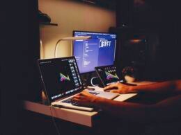 Frau in schwarzem Top sitzt konzentriert vor einem Computer im modernen Arbeitsumfeld