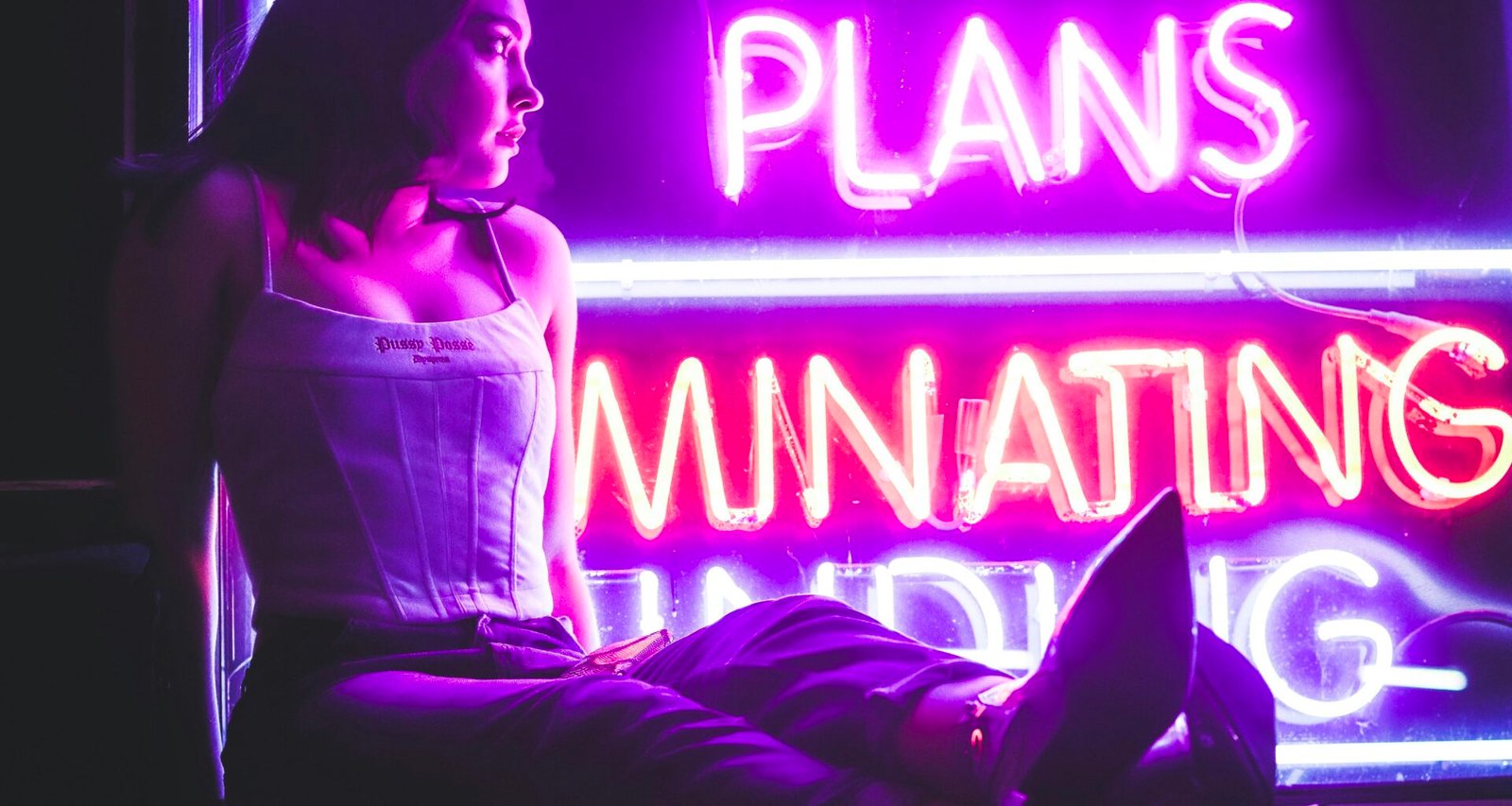 Frau mit weißem langen Shirt sitzt auf dem Fußboden in einem hellen Raum, Blick nach vorne gerichtet