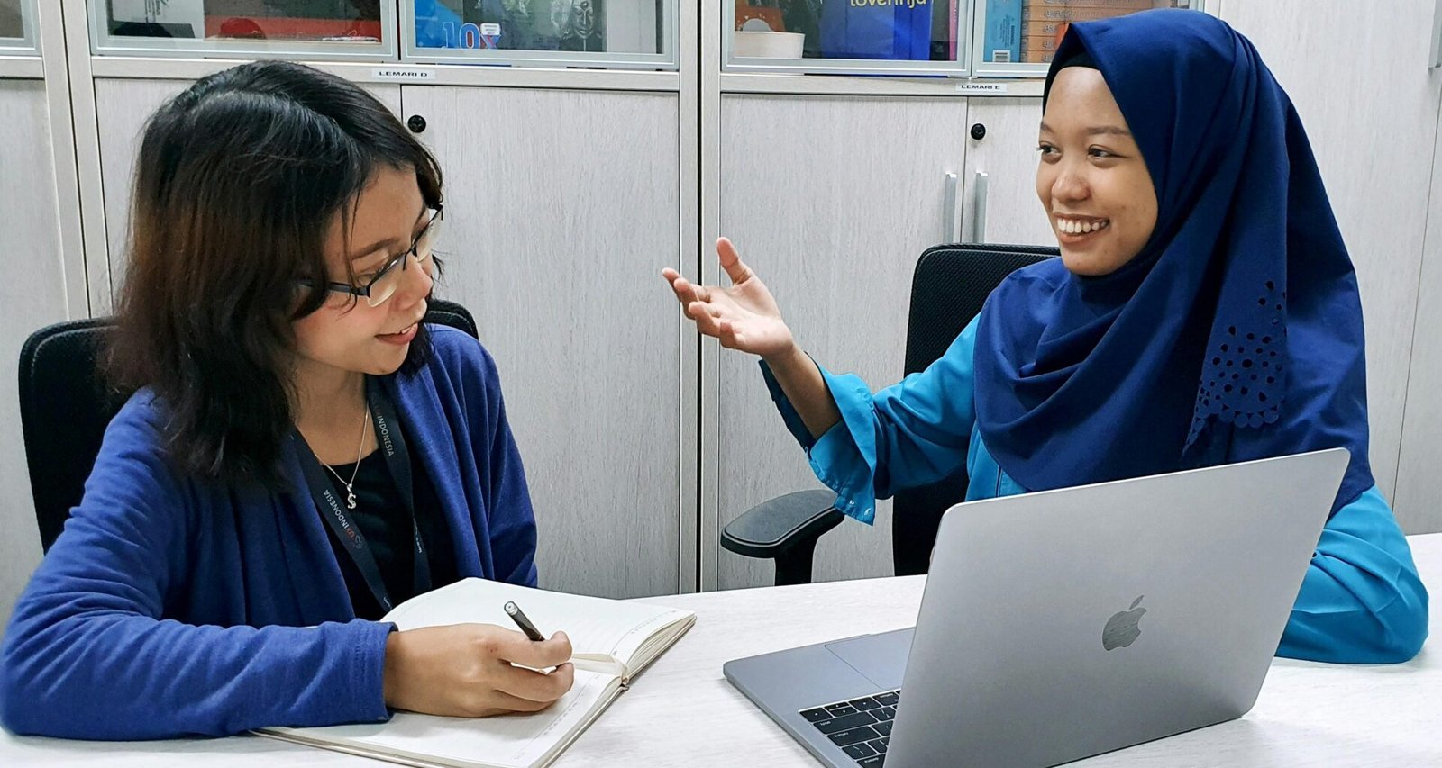 Frau in blauer Robe arbeitet konzentriert an einem MacBook an einem Tisch, geeignet für Themen wie Homeoffice und Technologie.