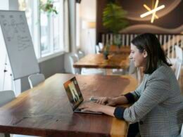 Frau mit grau-weiß gestreiftem Longsleeve arbeitet konzentriert an einem silbernen MacBook an einem Schreibtisch