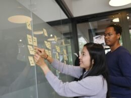 Frau im grauen Pullover hält ein goldenes iPhone 6 in der Hand und nutzt das Smartphone zur digitalen Kommunikation.