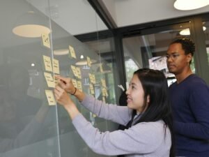 Frau in grauem Pullover hält ein goldenes iPhone 6 in der Hand und nutzt das Smartphone im Alltag.