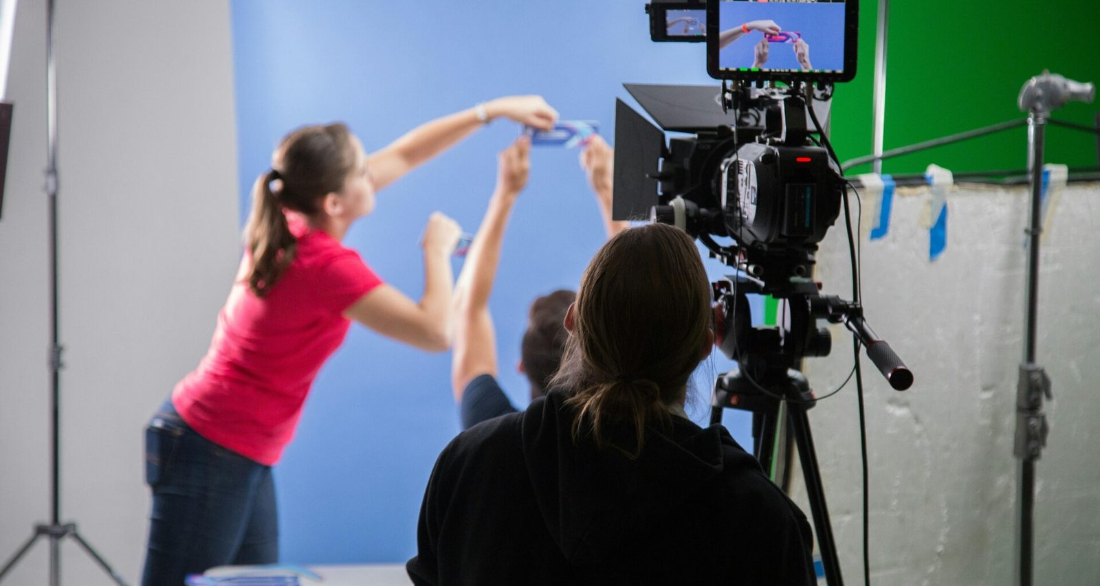 Eine Frau im pinken Langarmshirt hält eine schwarze Videokamera, Fokus auf technisches Interesse und Medieneinsatz.