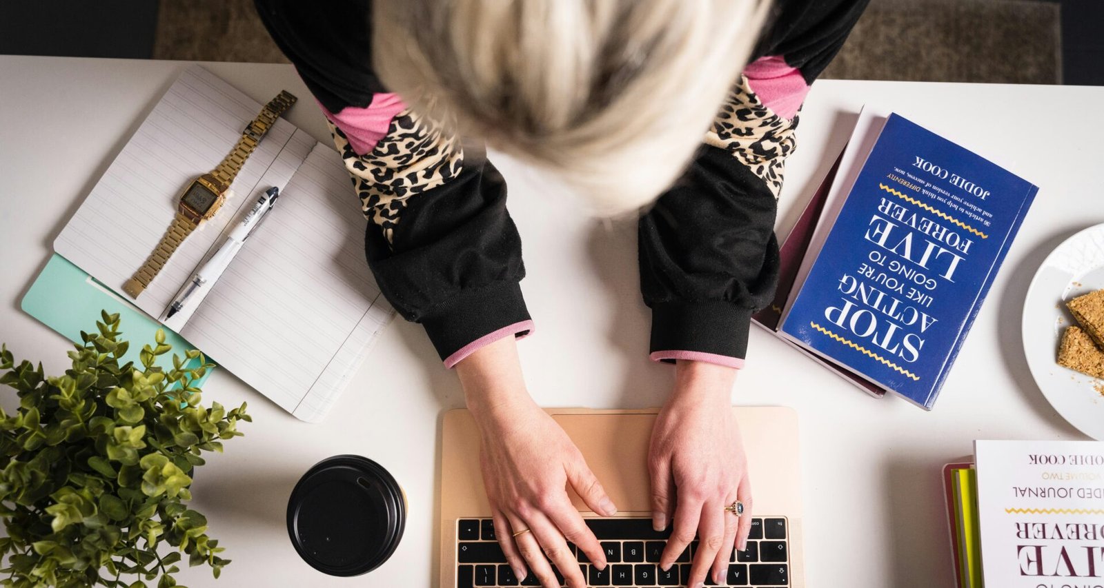 Frau mit schwarzem und pinkem Langarmshirt arbeitet an einem MacBook Pro an einem Schreibtisch in moderner Umgebung.