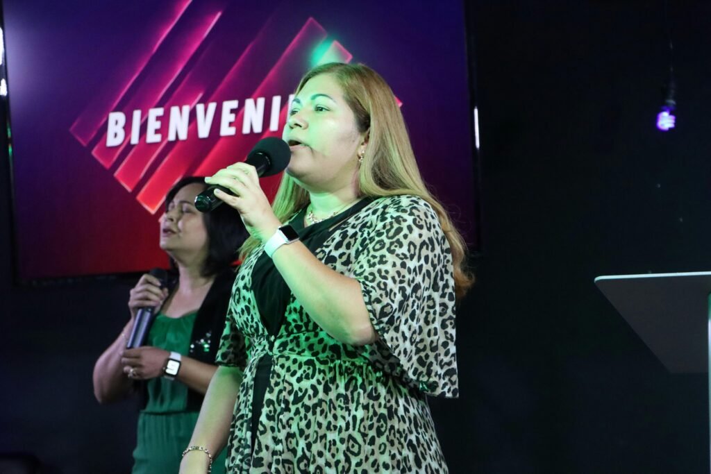 Frau in schwarz-weißem Leopardenkleid singt auf einer Bühne mit Mikrofon und Bühnenbeleuchtung