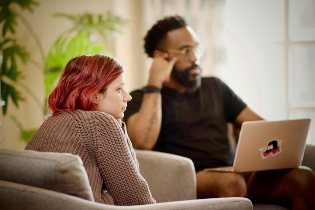 Frau in schwarzem Shirt sitzt auf braunem Stuhl vor neutralem Hintergrund, Fokus auf Arbeitsumfeld