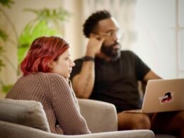 Frau mit schwarzem Shirt sitzt auf einem braunen Stuhl vor neutralem Hintergrund, Symbol für konzentriertes Arbeiten im Büroalltag