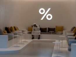 Frau mit weißem Langarmshirt und schwarzer Hose sitzt auf weißem Stuhl in heller Umgebung