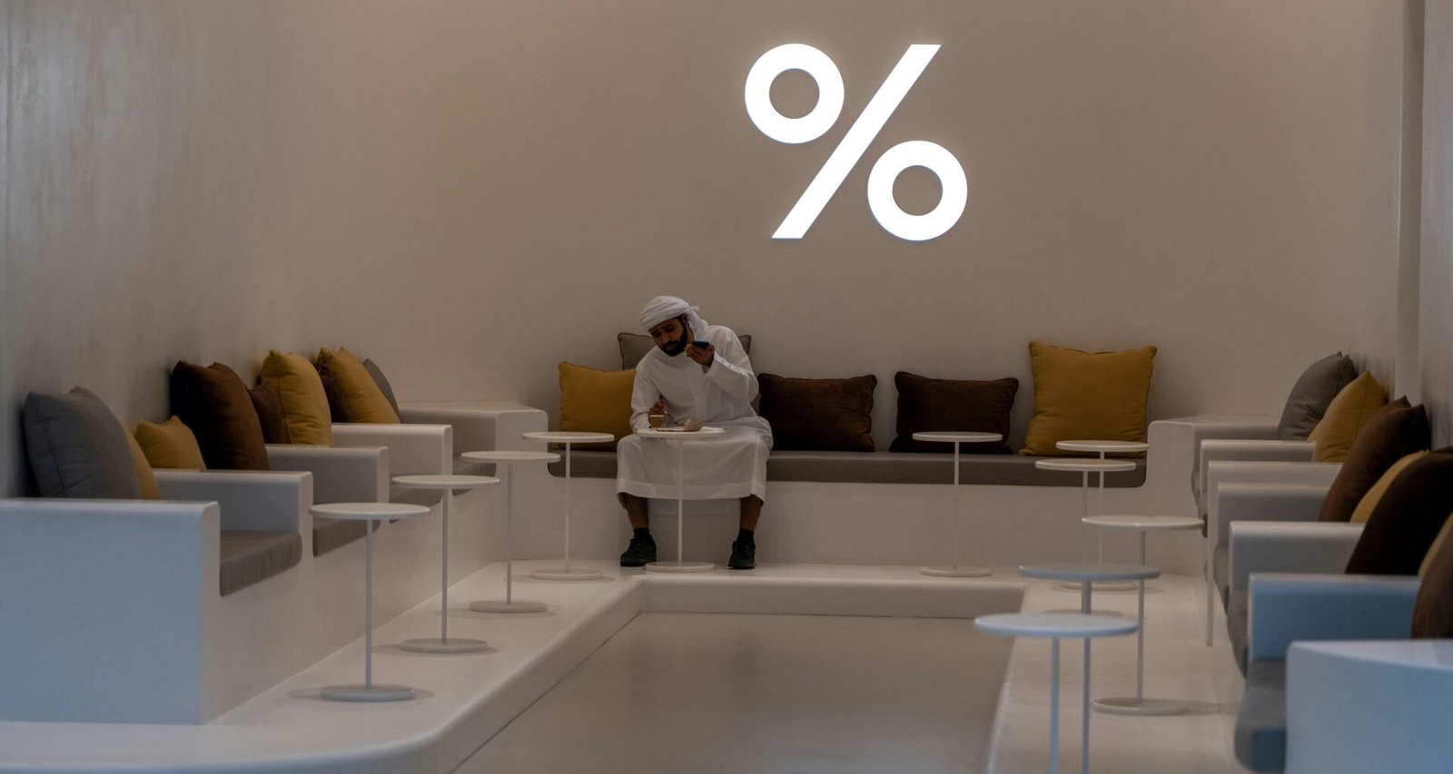 Frau mit weißem Langarmshirt und schwarzer Hose sitzt entspannt auf einem weißen Stuhl vor hellem Hintergrund