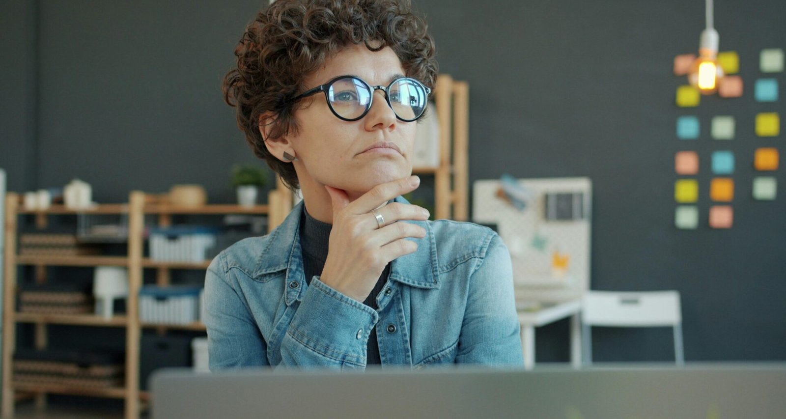 Frau mit Brille sitzt am Schreibtisch und denkt nach, Fokus auf Produktivität und moderne Arbeitsumgebung