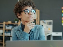 Frau mit Brille sitzt am Schreibtisch und denkt nach, Fokus auf Produktivität und moderne Arbeitsumgebung