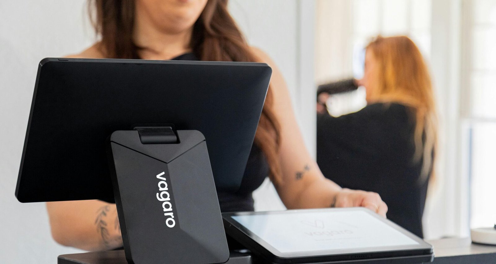 Frau arbeitet mit einem Tablet am Kassentresen eines Geschäfts und bedient Kundenzahlungen digital am Point of Sale.