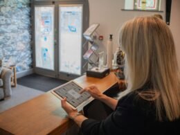 Frau nutzt ein Tablet an einem Empfangsschalter im modernen Büro. Fokus auf digitale Arbeitsweise und Technologie.