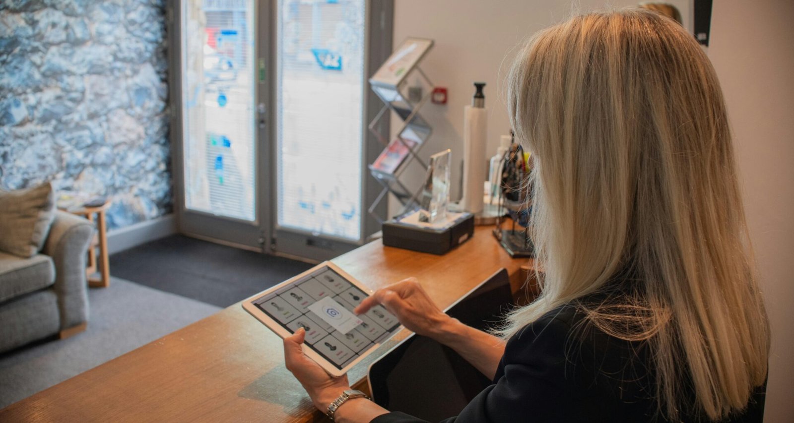 Frau nutzt ein Tablet an einem Empfangstresen, um digitale Prozesse zu unterstützen, fotografiert von Bluestonex